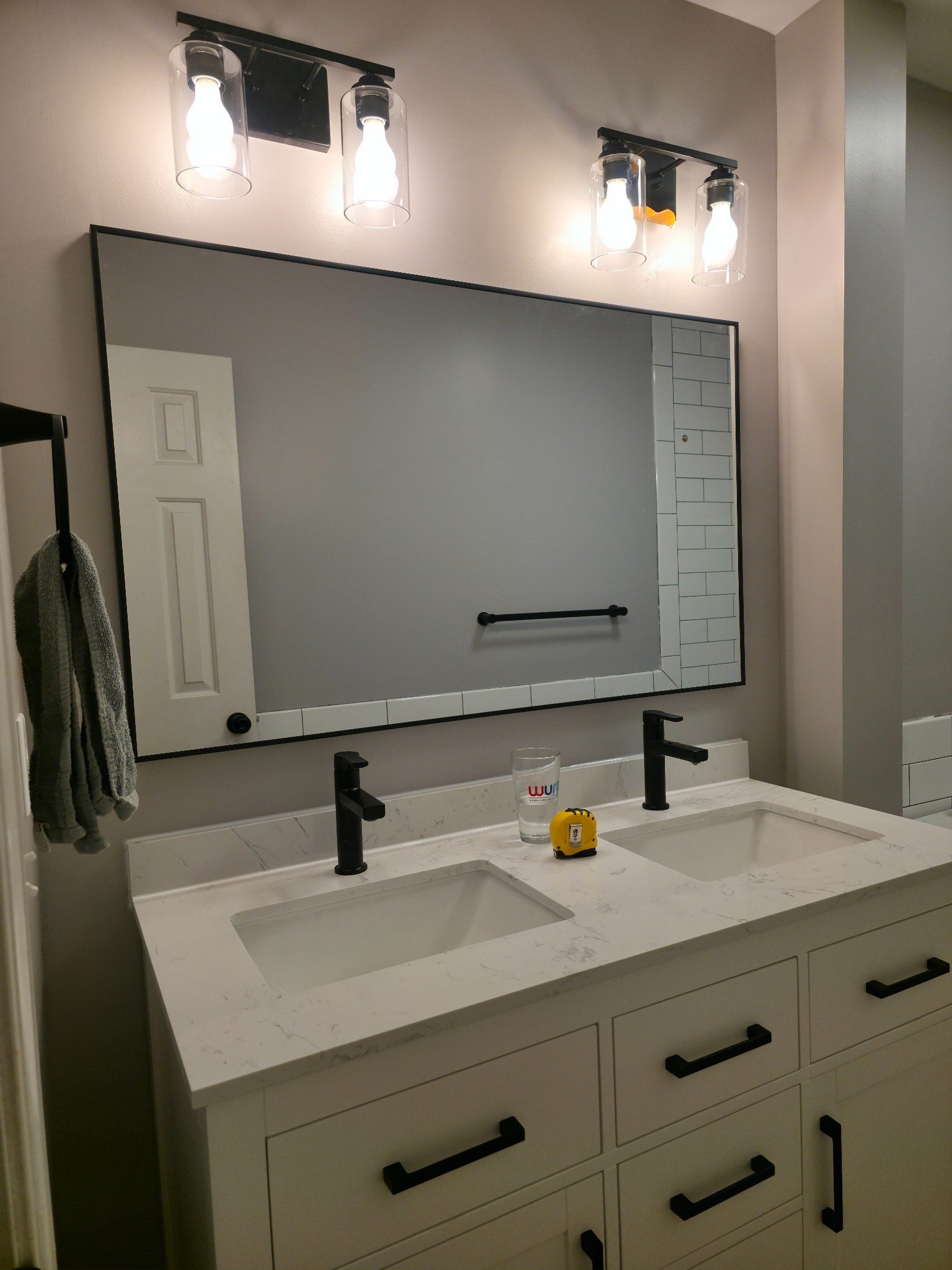 Completed bathroom vanity with white shaker cabinets, quartz countertop, matte black faucets, and black-framed mirror in Carrboro NC
