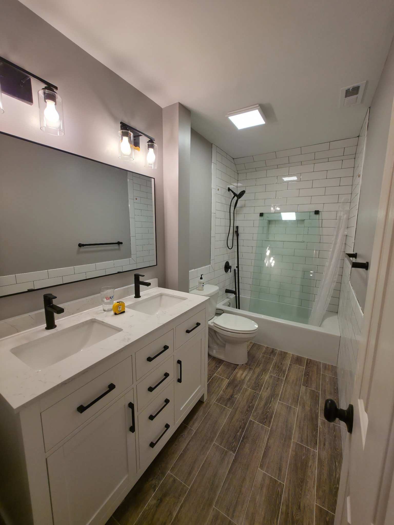 Completed bathroom remodel with white shaker vanity, quartz countertop, subway tile surround, and sliding glass door in Carrboro NC