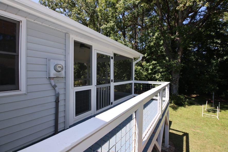 Exterior side view of completed screened porch addition showing roof tie-in and wire railing in Durham NC