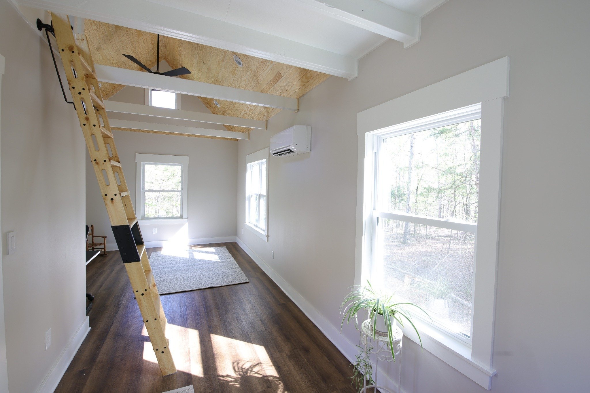 Interior of completed office shed showing mini-split HVAC unit, loft ladder, and hardwood floors in Durham NC
