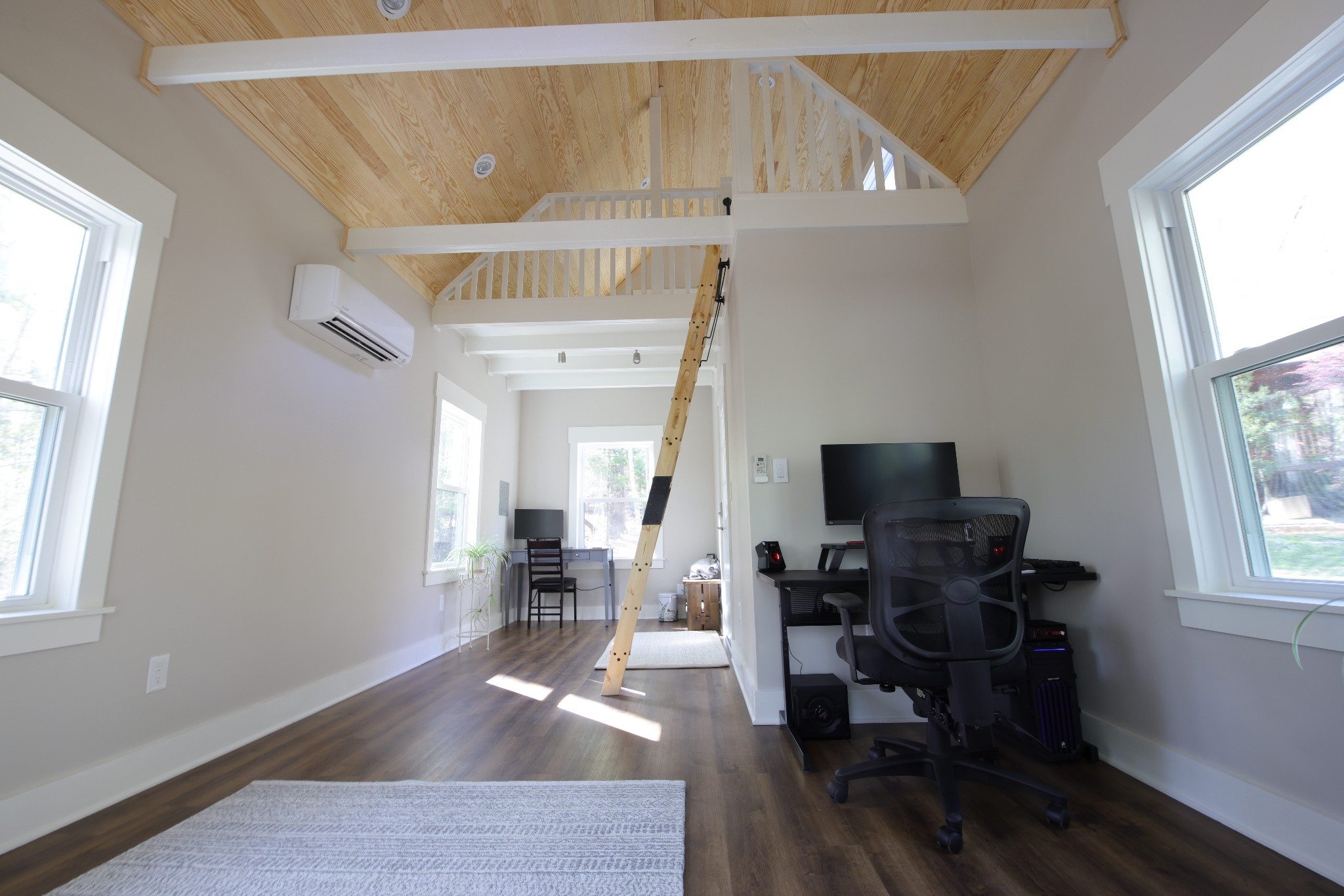 Wide interior view of finished office shed showing dual workstations, loft, and vaulted wood ceiling in Durham NC