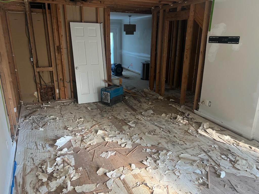 First floor walls stripped to studs with drywall debris and air movers during remediation demo in Raleigh townhouse