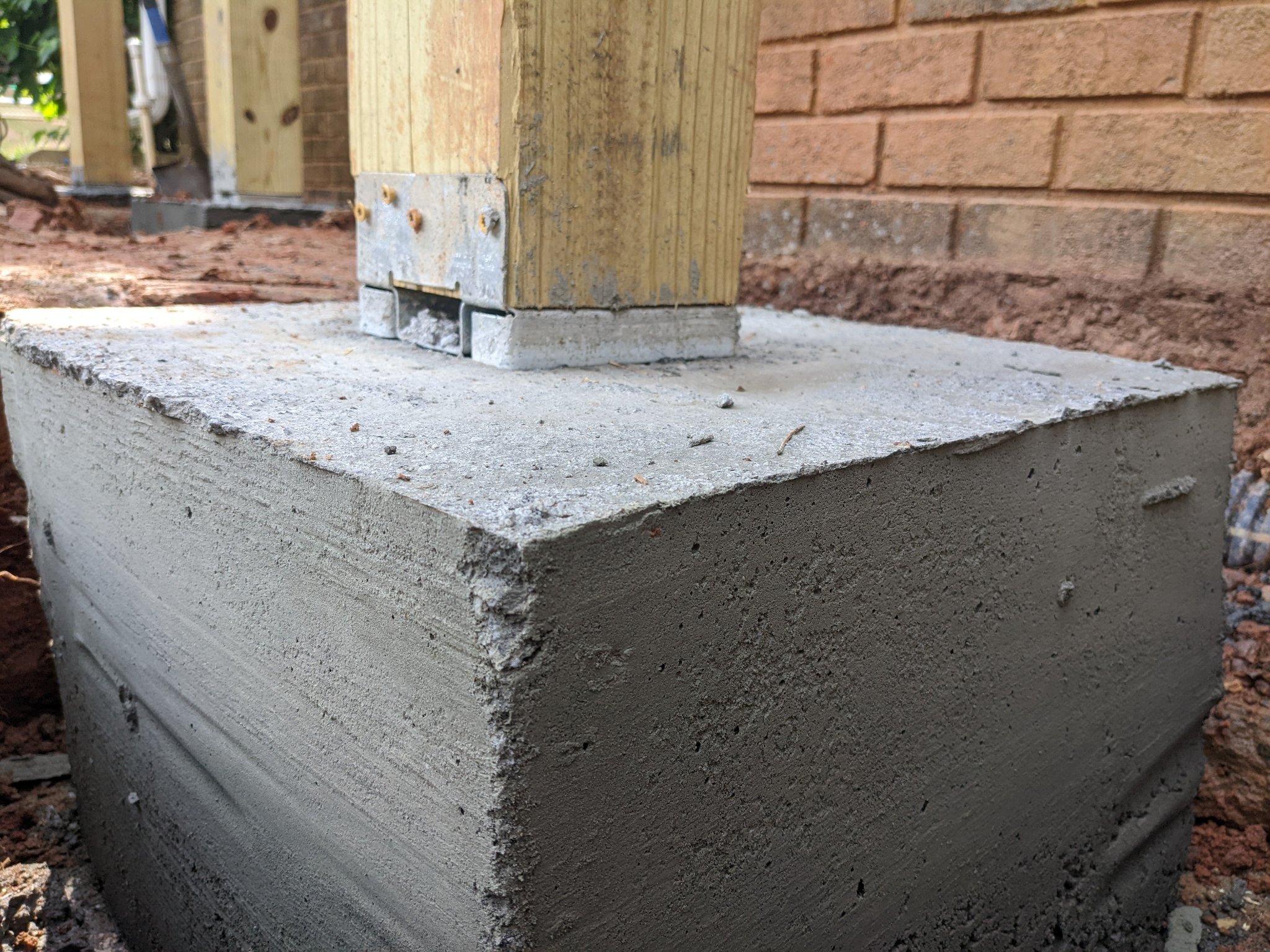 Close-up of poured concrete footing with post base hardware for deck in Raleigh NC