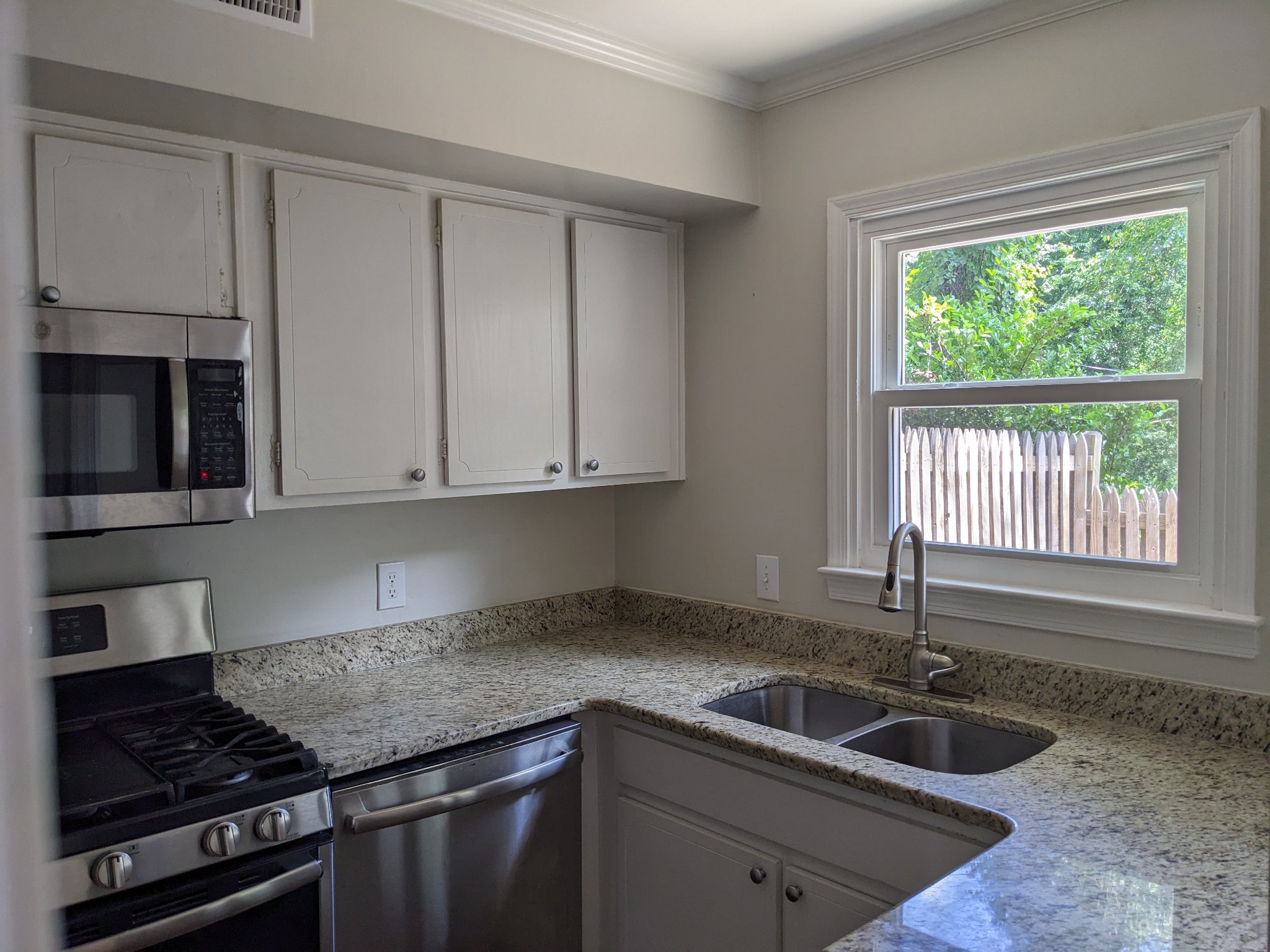 Original kitchen corner with white cabinets, granite counters, and window before remodel in Raleigh townhouse